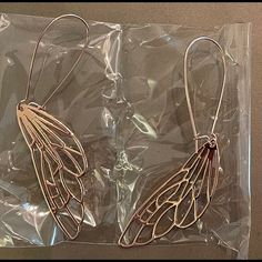 two pairs of earrings sitting on top of a plastic wrapping bag in the shape of wings