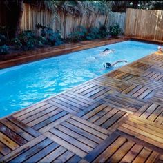 an empty swimming pool with wooden decking around it and people in the water below