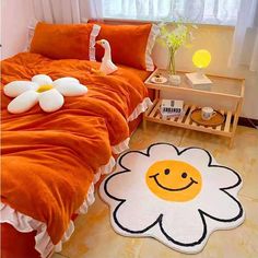 a bed with an orange comforter and a white flower rug on the floor next to it