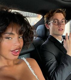 a man and woman sitting in the back seat of a car with their hands up