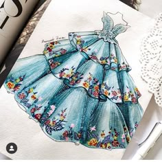 a drawing of a blue dress on top of a white doily next to a lace doily