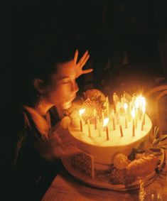 a woman blowing out candles on a cake with her hands in front of the cake