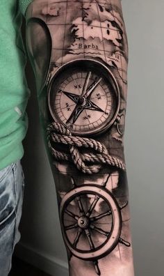 a man's arm with a compass and ship wheel tattoo on the left forearm