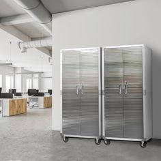 two stainless steel refrigerators sitting in an empty office space with desks and chairs