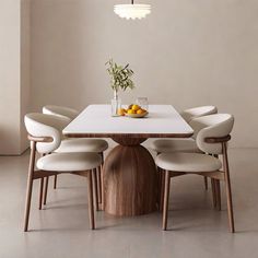 a dining table with four chairs around it and a vase filled with fruit on top