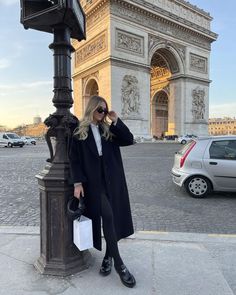 a woman standing next to a lamp post in front of the arc de trioe