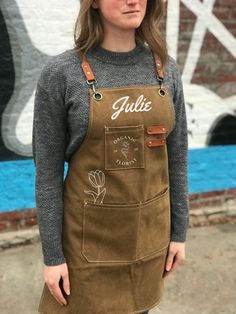 a woman standing in front of a graffiti wall wearing an apron with the word julia on it