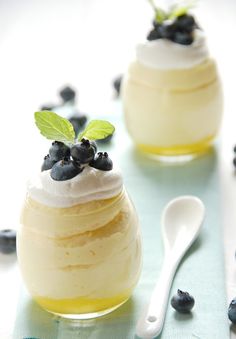 two desserts with blueberries and whipped cream are on a table next to a spoon