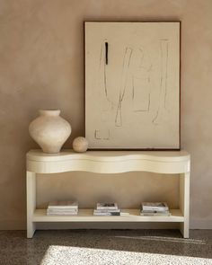 a white shelf sitting next to a painting and vase on top of a table in front of a wall