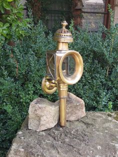 an old fashioned lamp on top of a rock in front of some bushes and trees