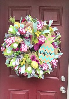 a colorful wreath with the word welcome hanging on a red door that is decorated with green, yellow and pink ribbons