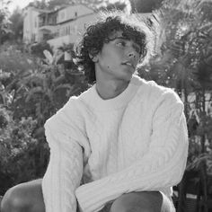 black and white photograph of a young man sitting on a bench in front of trees