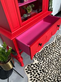 a red hutch sitting on top of a rug next to a potted plant