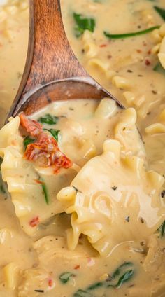 a wooden spoon filled with pasta and spinach in a creamy broccoli sauce