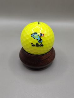 a yellow golf ball sitting on top of a wooden stand that says too heeezs