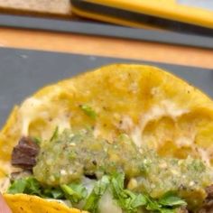 a hand holding a taco filled with meat, cheese and cilantro sauce