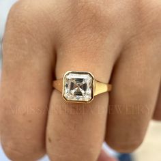 a woman's hand wearing a gold ring with an emerald stone in the center