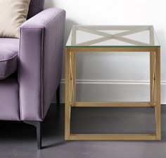 a purple chair next to a glass table with gold trim on it and a white wall in the background