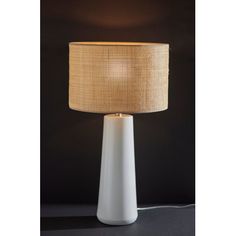 a white table lamp with a beige shade on it's side and a black wall in the background