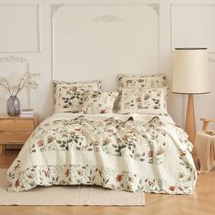 the bed is made with floral comforters and pillows on top of wooden flooring