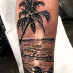 a man's arm with a palm tree and ocean scene on it, while the sun is setting