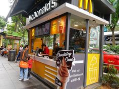 a mcdonald's ice cream stand on the side of a street with people standing outside