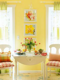 two chairs and a table in a room with yellow walls, white trim and windows