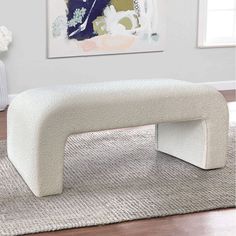 a white bench sitting on top of a rug in front of a wall mounted painting