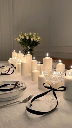 a table topped with lots of white candles next to plates and silver utensils