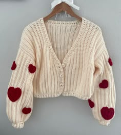 a cardigan sweater with hearts on it hanging from a hanger against a wall