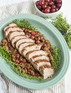 a green plate topped with meat and beans next to a bowl of grapes on top of a table