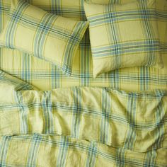 an unmade bed with yellow and blue plaid sheets, pillows and pillowcases