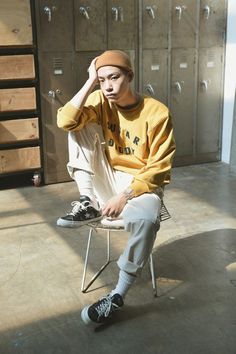 a young man sitting on top of a metal chair in front of lockers wearing a hat