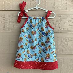 a blue dress with red polka dots and bicycles on it, hanging from a hanger