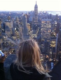 a woman standing on top of a tall building looking at her cell phone in the city