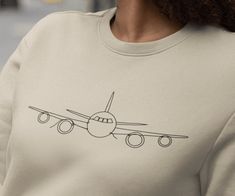 "Takeoff in style. This minimalist airplane line drawing graphic shirt is perfect for the traveler or pilot! Gift this aviation t-shirt to that special someone who travels a lot and explore everything there is to see. Soft and comfortable classic fit crewneck sweatshirt. For an oversized look size up. Size:  See product photos for size chart Material:  - Preshrunk fleece knit - Air jet yarn, softer feel and reduced pilling - Double-needle stitching at shoulder, armhole, neck, waistband, and cuffs - 1 x 1 rib with spandex - Quarter-turned to eliminate center crease - Classic fit - Tear away label Care Instructions: - Machine wash at a low heat. - Wash garments inside-out, with similar colors. - Avoid using bleach. Use non-chlorine bleach if necessary. - Do not use fabric softeners. - Tumble Airplane Shirt, Ideas Regalos, Drawing Graphic, Pilot Gifts, Airplane Mode, Shirt Embroidery, Cabin Crew, Cozy Fits, Travel Lover