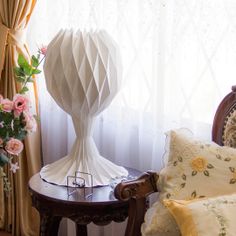 a white vase sitting on top of a wooden table next to a chair and window