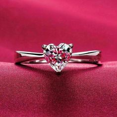 a heart shaped diamond ring on a pink cloth