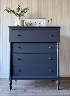 a blue dresser with gold handles and knobs on it's sides, in front of a striped wall