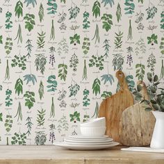 a wooden table topped with white plates and green leaves wallpapered behind a cutting board