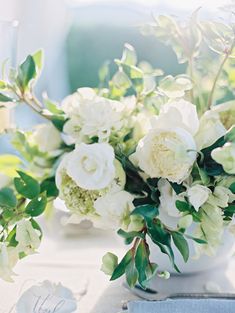 white flowers and greenery are in a vase on a table with silver utensils