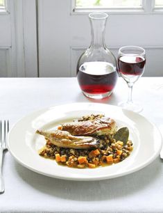 a white plate topped with meat and vegetables next to a glass of wine on a table