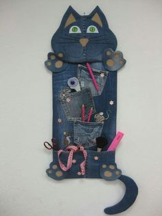 a cat made out of jeans with scissors and pencils in its pocket, hanging on the wall