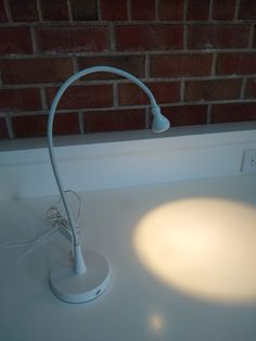 a white desk lamp sitting on top of a table next to a brick wall and window