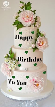 a three tiered cake with flowers and hearts on the top is happy birthday to you