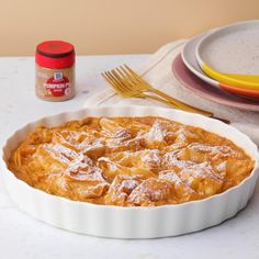 a pie dish with powdered sugar on top sits next to plates and a fork