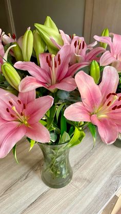 a vase filled with pink lilies on top of a wooden table next to a mirror