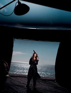 a woman standing on top of a black tarp next to the ocean with her hair blowing in the wind