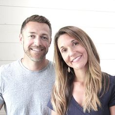 a man and woman standing next to each other in front of a white wall smiling at the camera