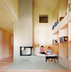 two children are sitting on the floor in front of an open fire place and bookshelf